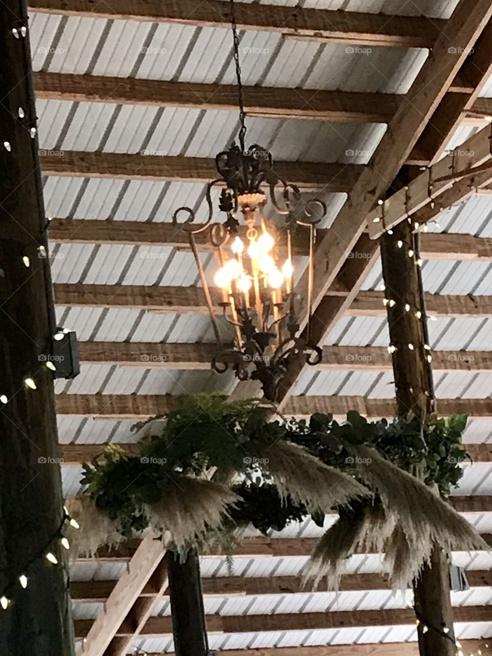 A vintage chandelier with fall foliage hanging from a barn ceiling