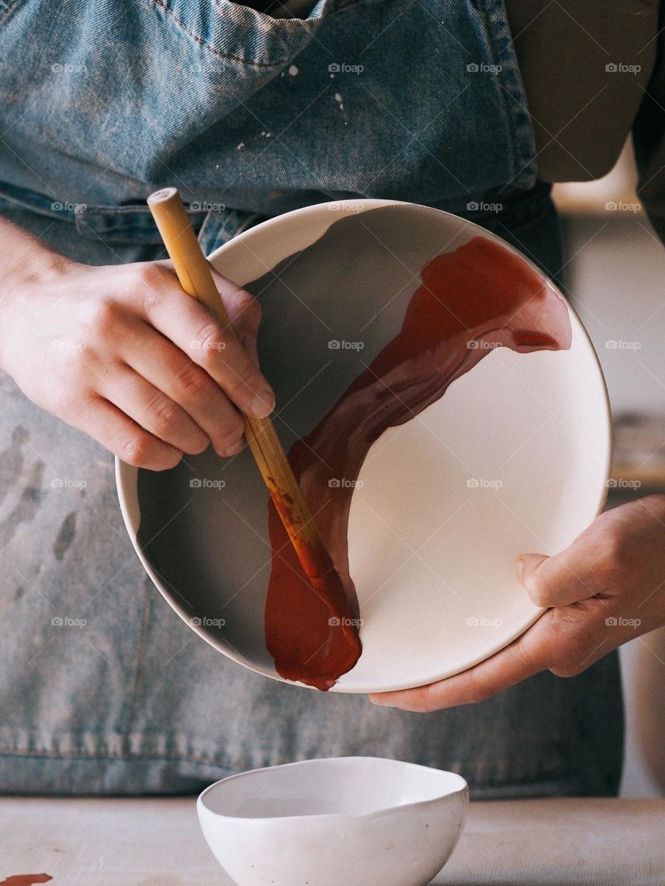 Unknown girl ceramist holding a round plate, covering it with glaze, crop photo, circle 