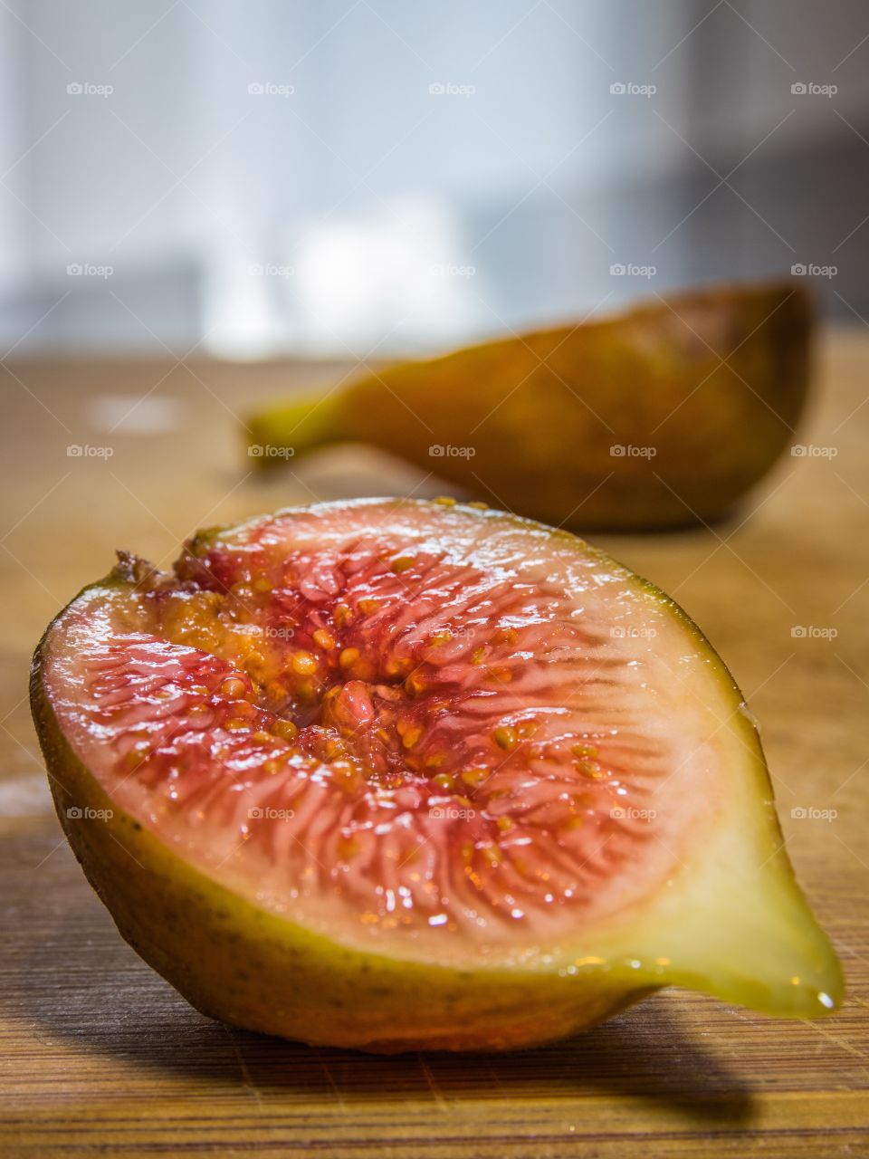 Vertical close up of the inside of half a fig on a wooden cutting board on a kitchen counter with the other half in soft focus in the background