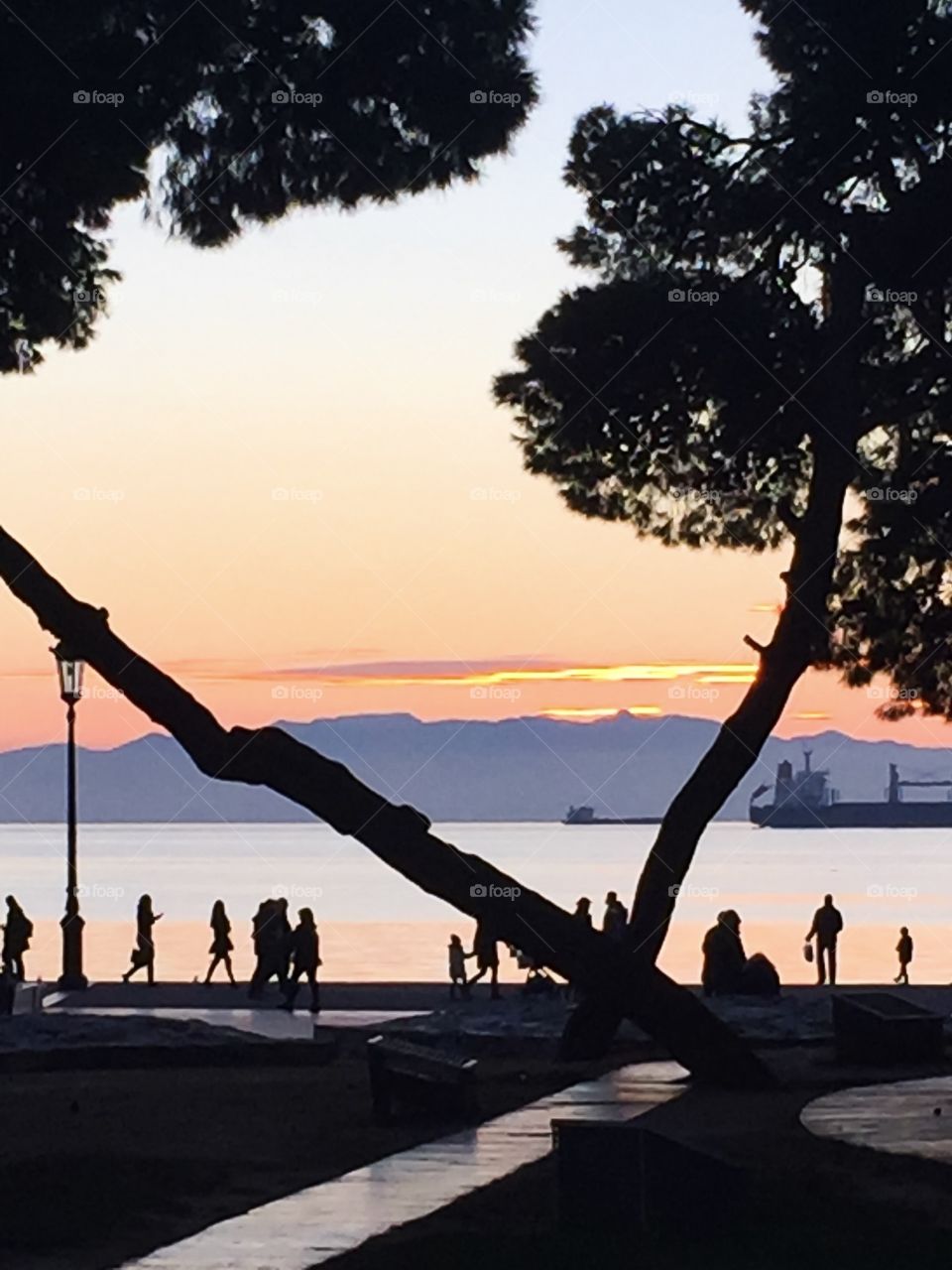 Silhouettes of people strolling along the embankment at sunset