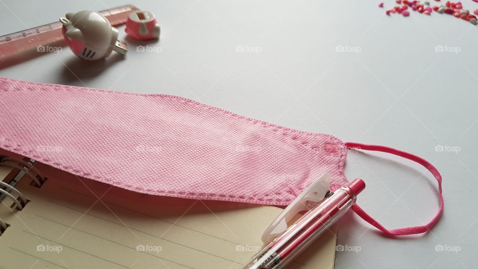 pink mask, pink pen, pink ruler, pink flash drive, and pink marbles, all on desk together..