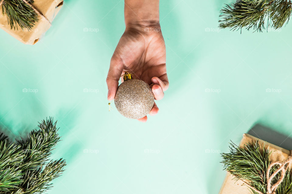 Christmas gift lying on green background. Female hand holding gold ball. Flatlay items. Flat lay, top view, surprise, happy new year, merry, tree, packing, packed, wrapping, celebrating, holidays, winter, background 