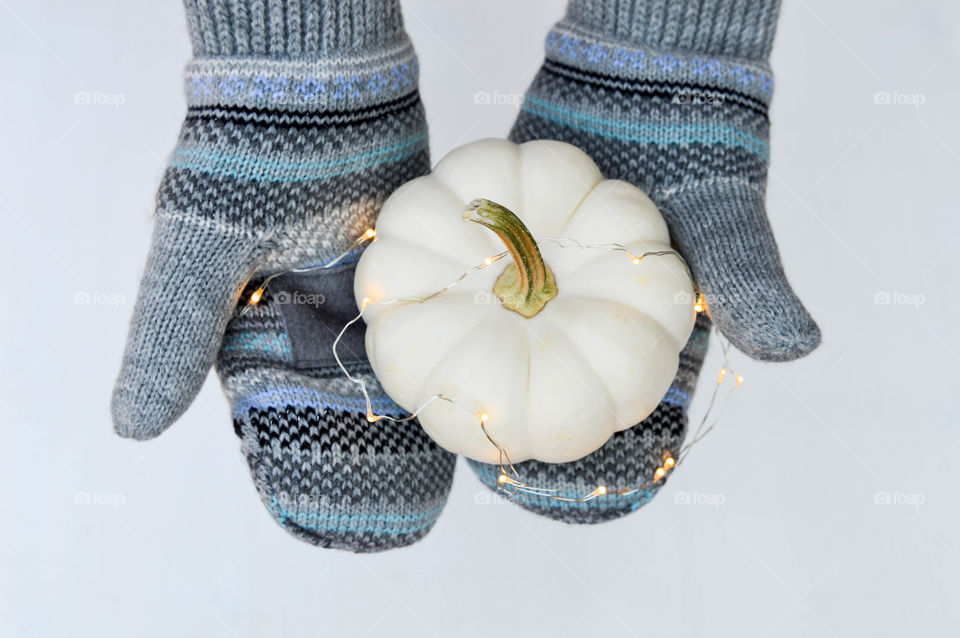 Close-up of a person's gloved hands holding a small white pumpkin wrapped in Christmas lights