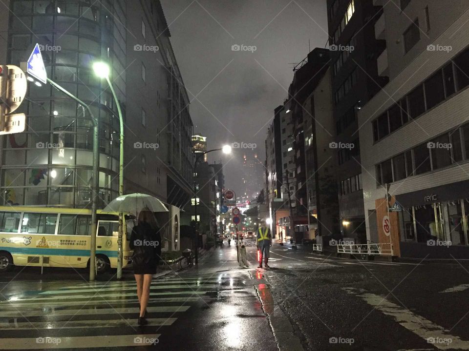 A street in tokio by night. A girl walking with an umbrella.