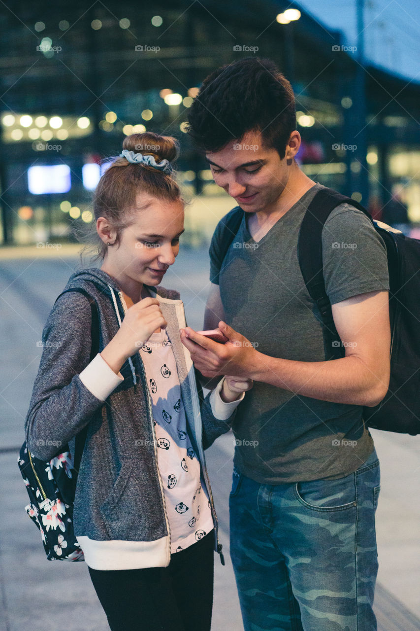 Young woman and man looking at screen of smartphone during walk in the city at night