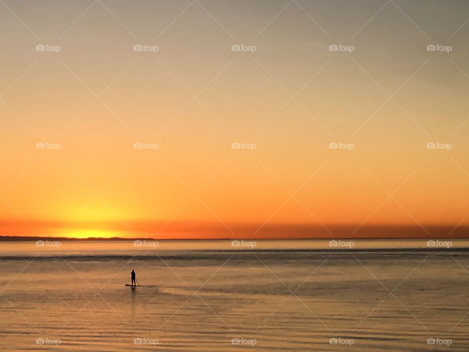 Paddle boarder silhouette on water in ocean at orange sky sunrise 