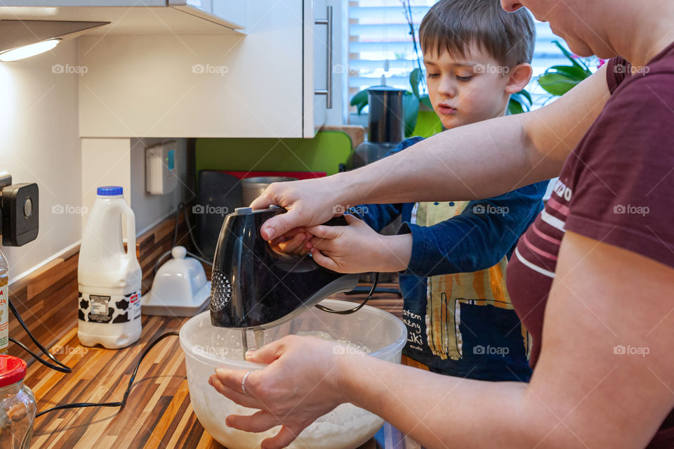 Little boy helps his mother making pancake mixture for breakfast.