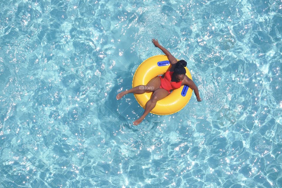 An African American woman floating on a pool float.