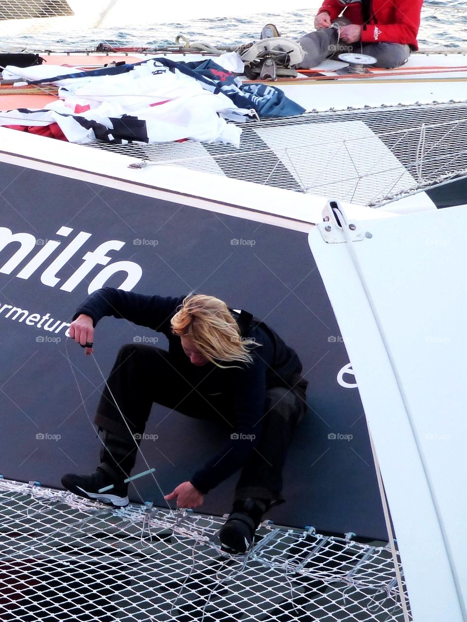 A woman repairs a sailboat before the start of a trimaran race