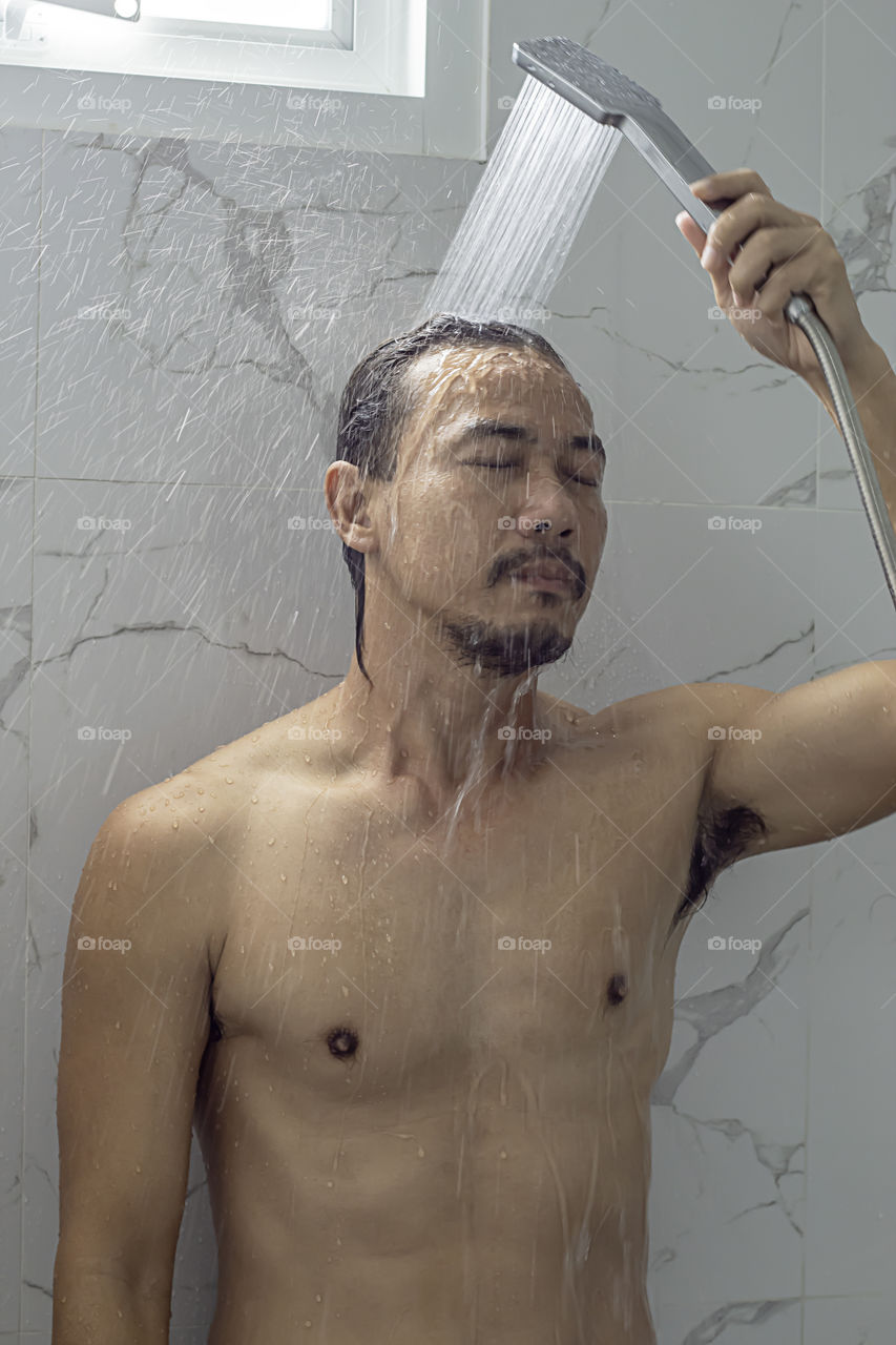Asian man taking a shower in the bathroom.