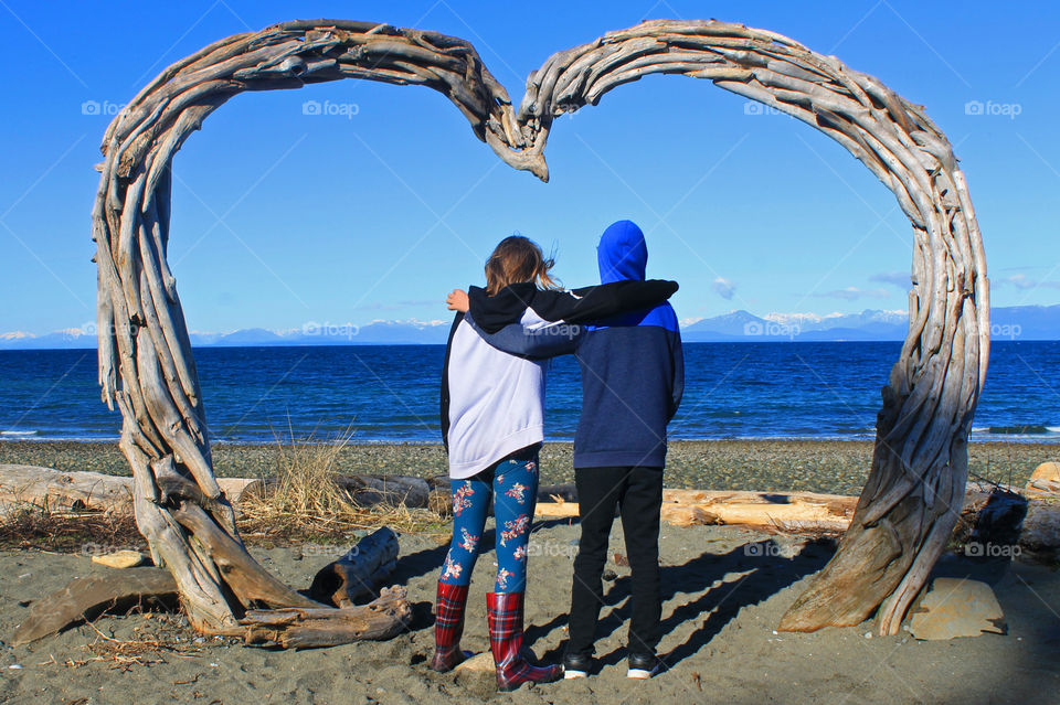 These young friends love to do everything together! They had a fun day & they stopped at the beach to look at the view from under the driftwood heart. They share a deep love of the beautiful blue ocean & mountains that surround their island home.