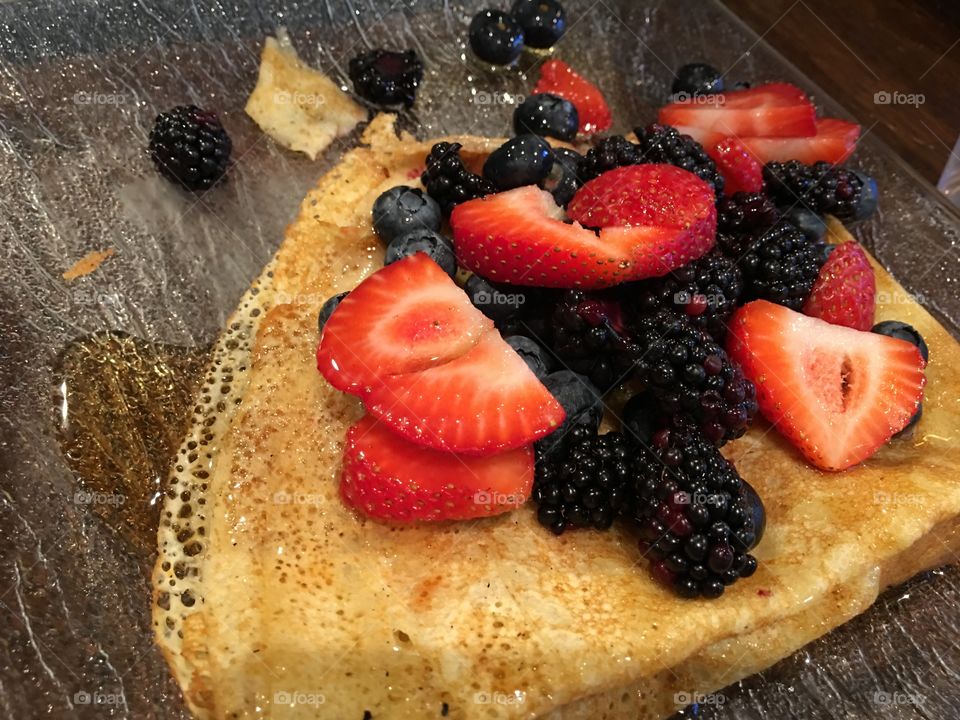 Beautiful fresh  antioxidant rich summer fruit on crepe with maple syrup berry types are Blackberry, Strawberry and blueberry on wood table surface 