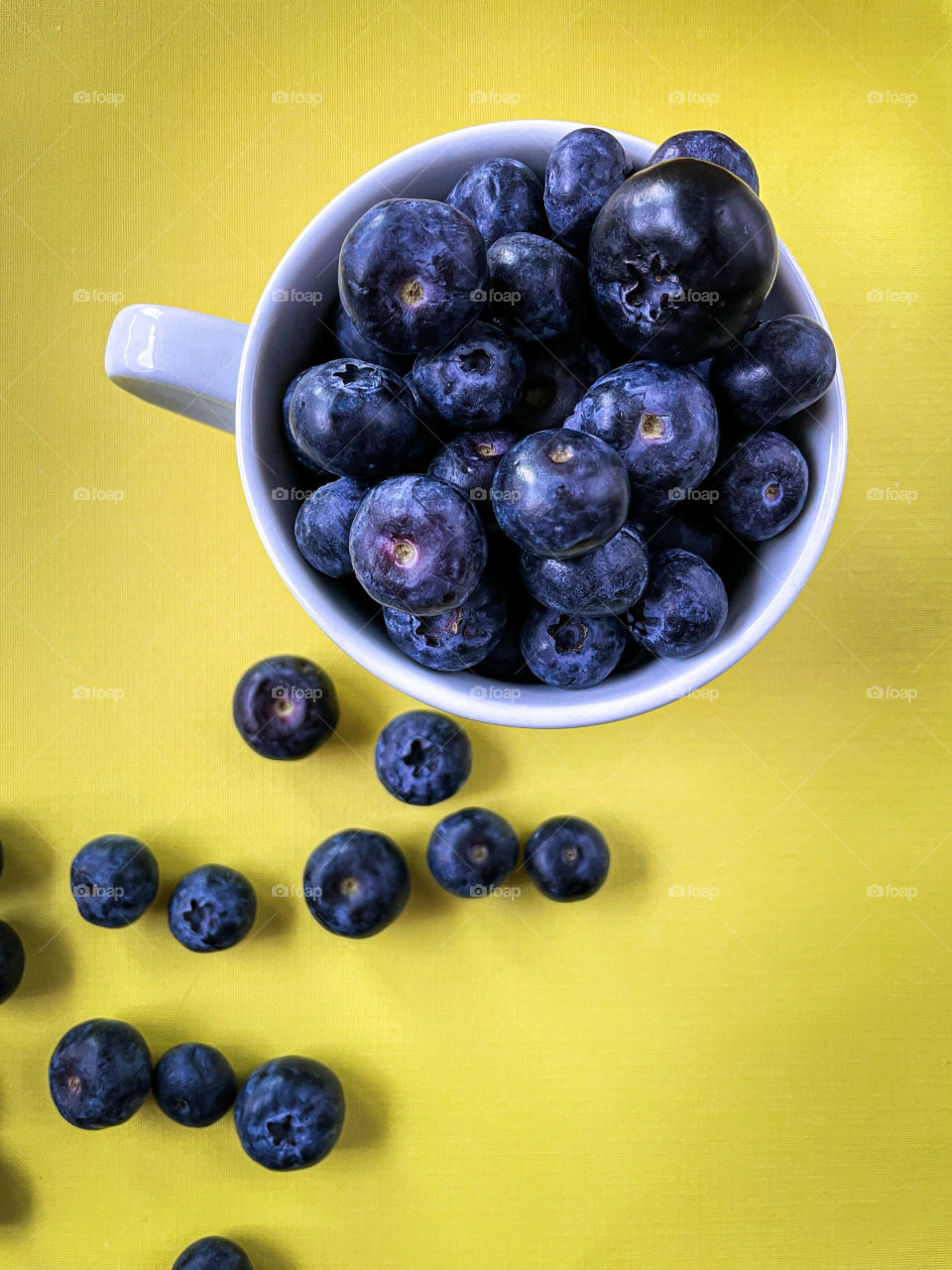 An overflowing cup of fresh, bright and healthy blueberries on a yellow background 