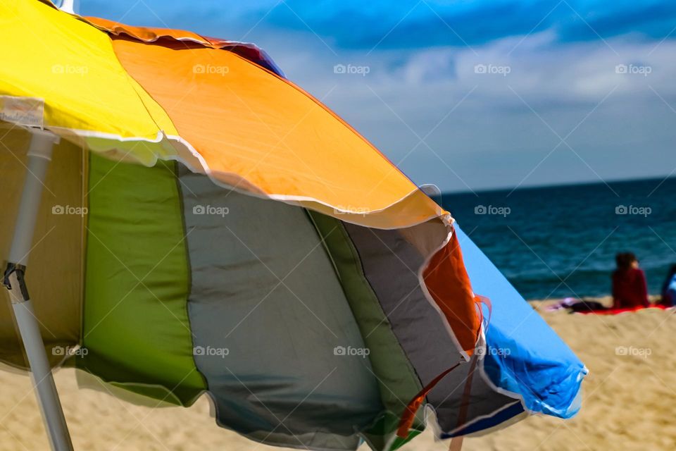 Colorful rainbow colored beach umbrella flapping in the wind on a warm summer day at the beach in Capitola California 