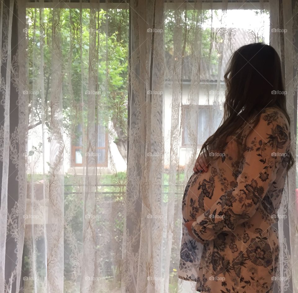 Pregnant young woman standing near window and waiting