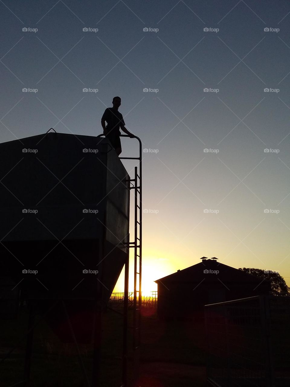 person on grain silo silhouetted against the setting sun