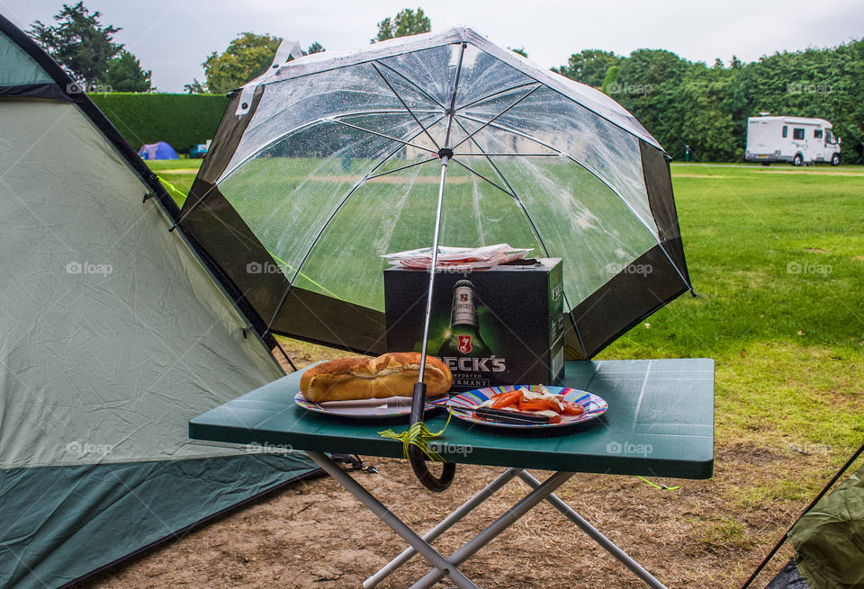 Camping during the Great British summer time - lager and picnic stashed securely under and umbrella at a campsite