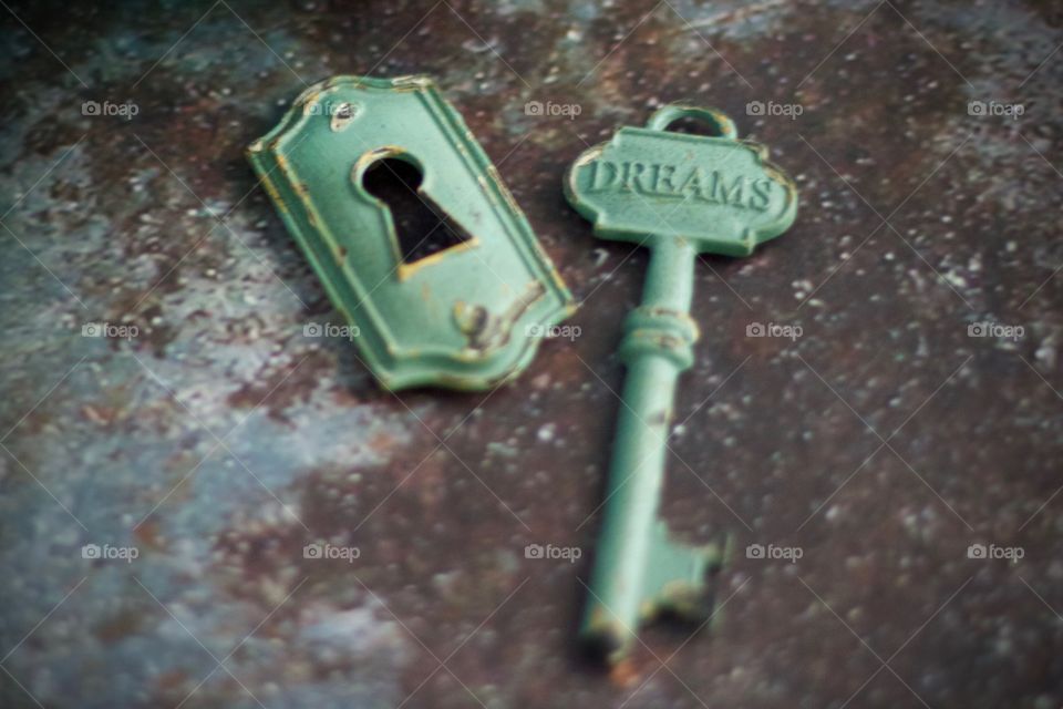 Light teal, metal vintage key with embossed word, “Dreams,” and keyhole on concrete surface 