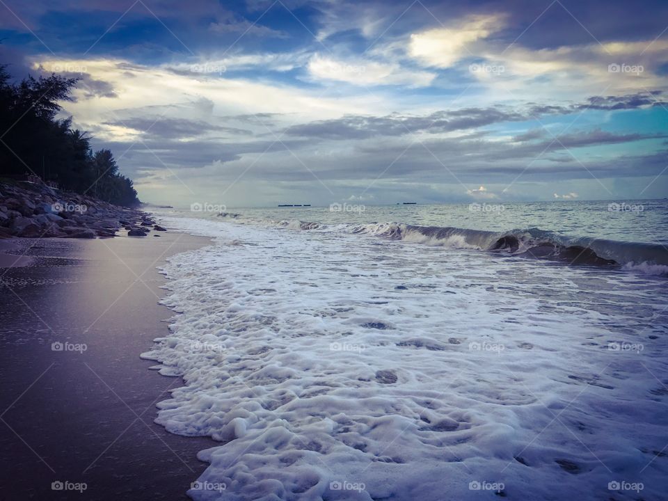 Cloudy sky in the evening above rocky beach licked by foamy tidal waves in southern Thailand