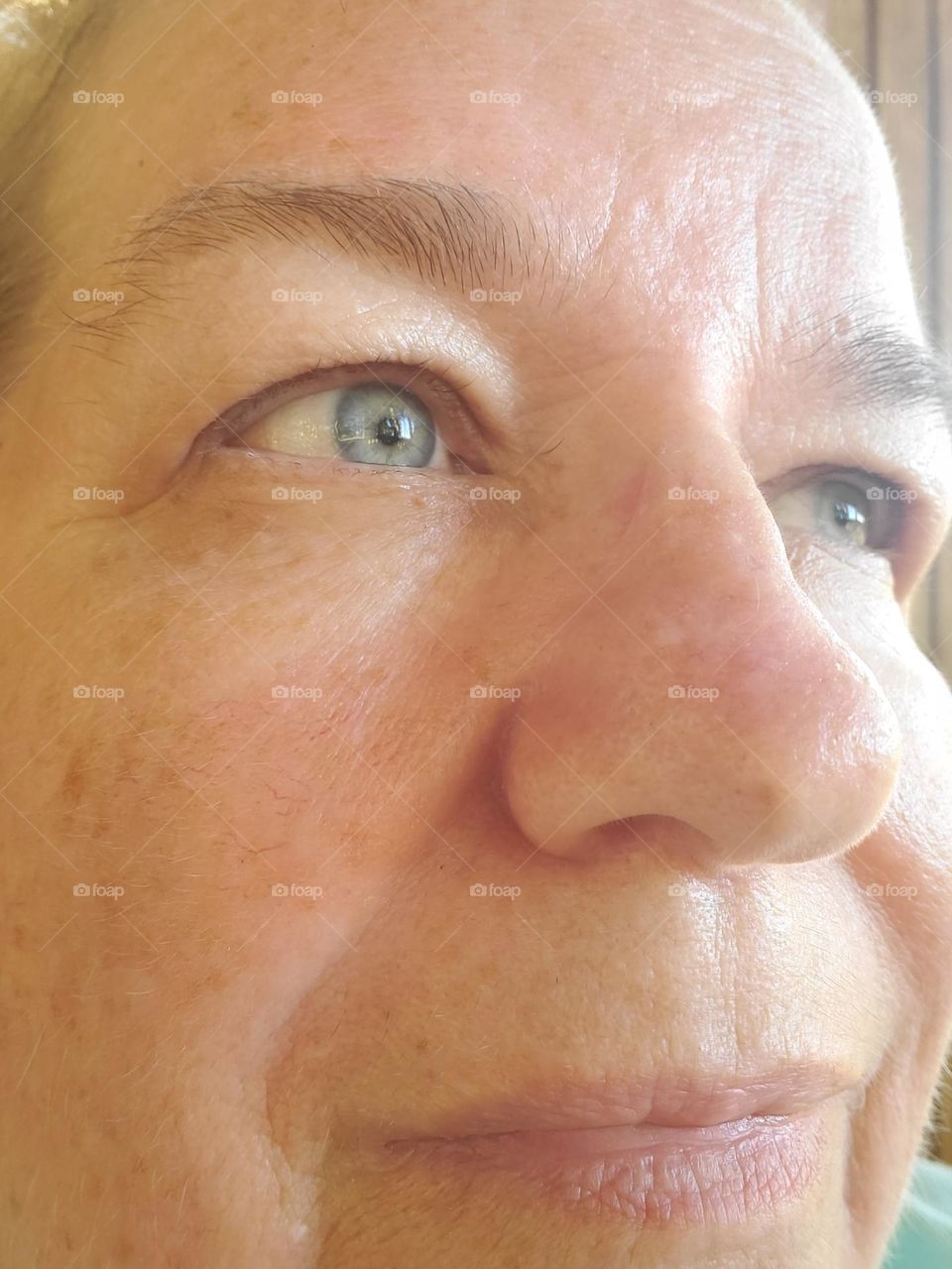 a smiling blue-eyed 63 year old woman who has no makeup on shows her unique face with her wrinkles, lines, age spots, rosacea and the scar from cancer on her nose