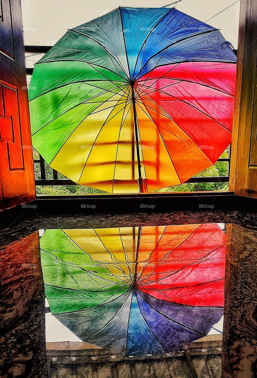 Reflection of a colorful umbrella on the glossy marble floor. The umbrella is kept just outside the door. Its reflections on the floor make an amazing, colorful environment. There was no water, oil, or any reflectionary fluid on the floor.