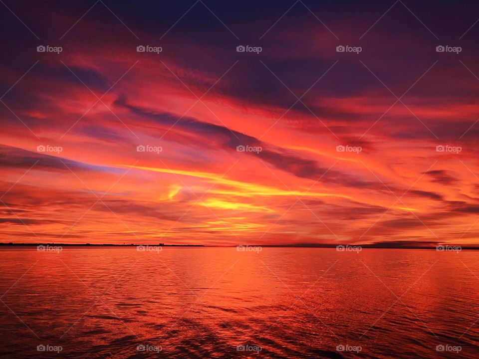 Mesmerizing sunset over the ocean with red, orange and mauve colored sky and
With an orange reflection on the waters surface. Colorful floating clouds over an open waterway