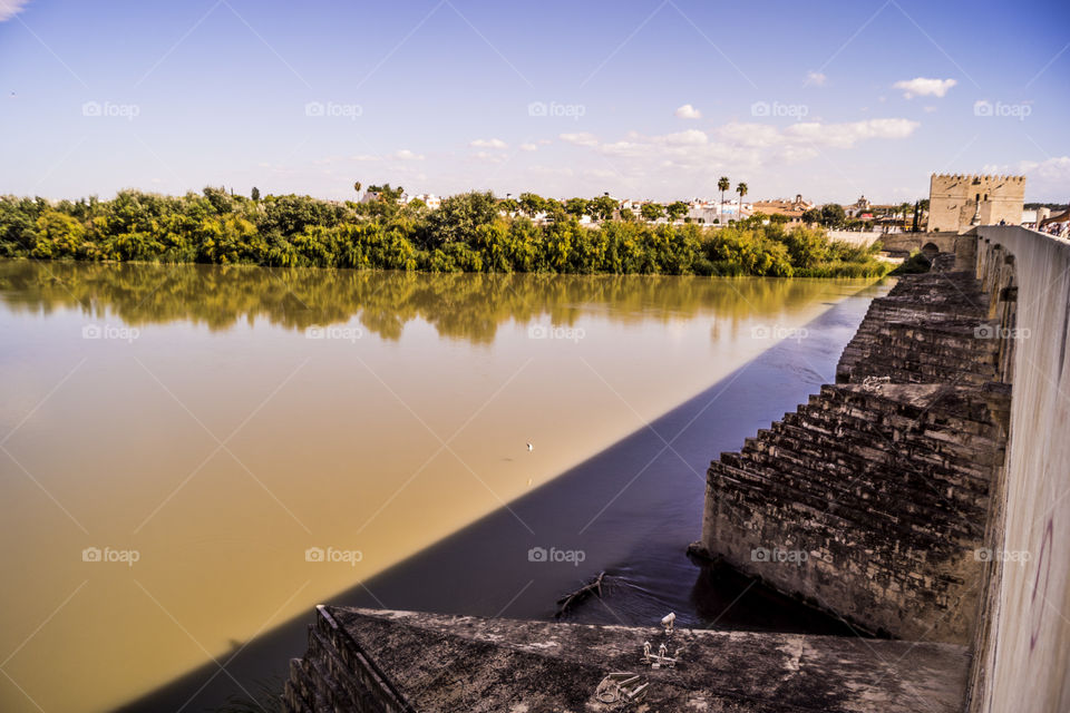 foto del río Guadalquivir desde el puente romano de Córdoba, Andalucía, dónde apreciamos la piedra con la que es construido y el paisaje que rodea las orillas del río.