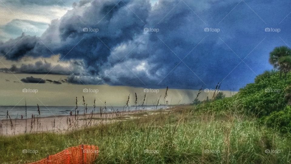 Scenic beach and dunes with beautiful blue ocean and ominous blustery rain clouds and steaks of rain moving across the horizon