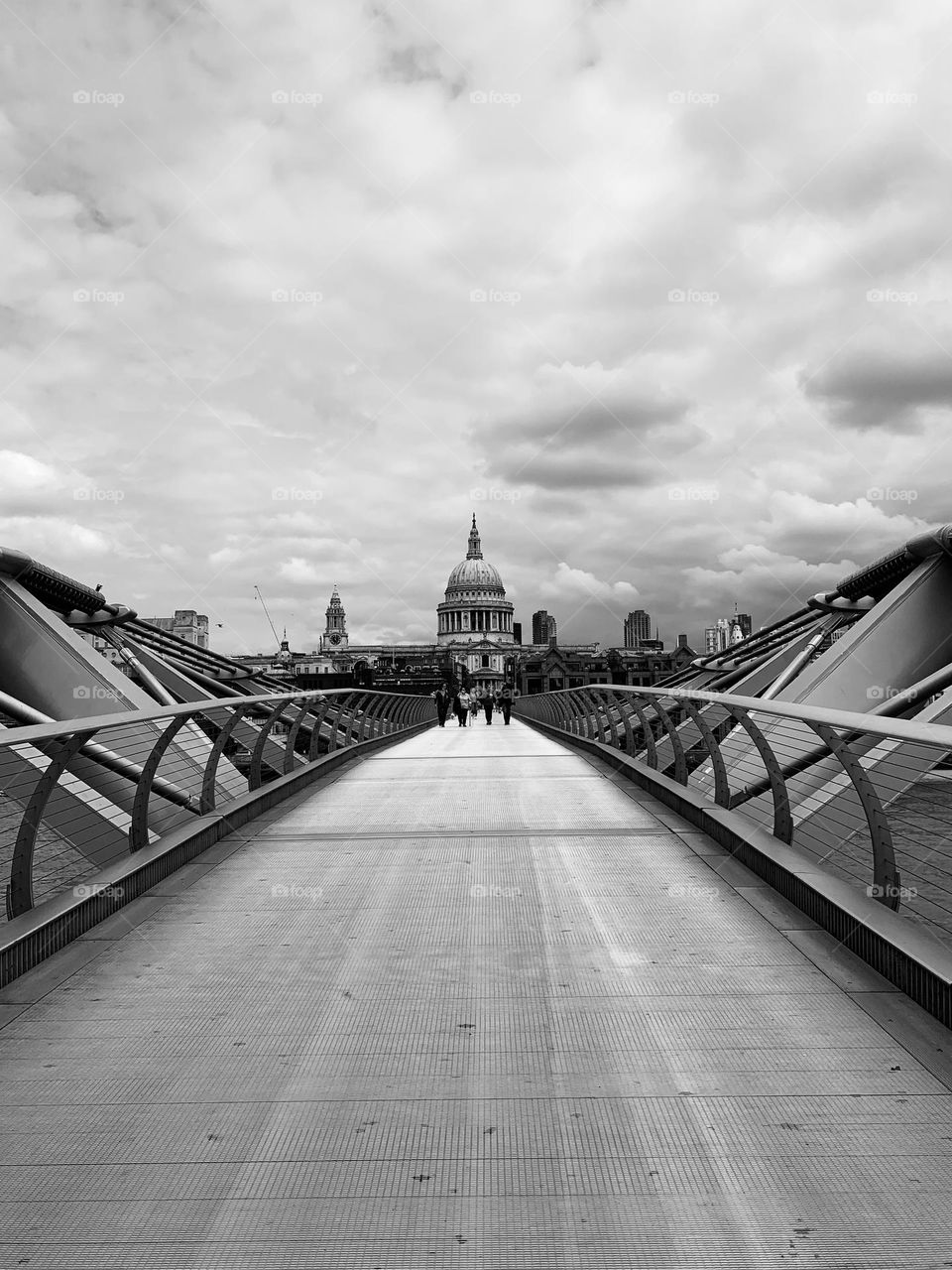 View of St Paul’s cathedral from south bank side of Millennium Bridge in London, UK, black and white, cloudy sky, unrecognizable people 