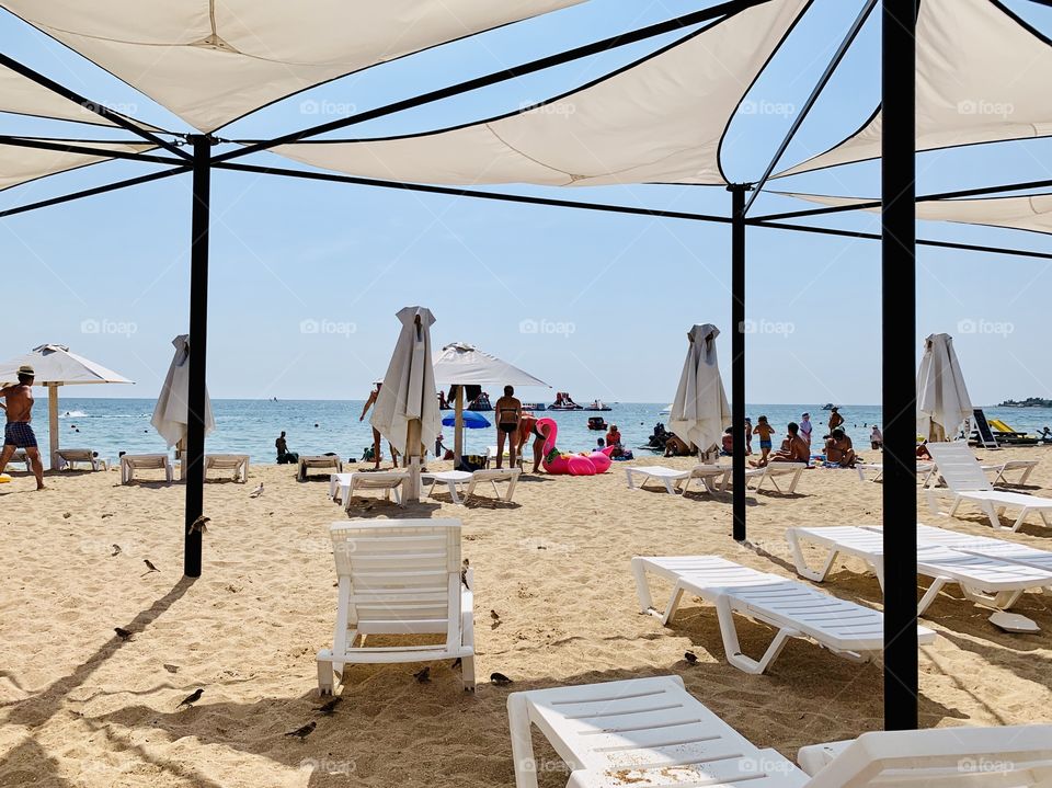 People relax on a sandy beach. White sun loungers, sun umbrellas, a rubber ring for swimming in the form of flamingos.