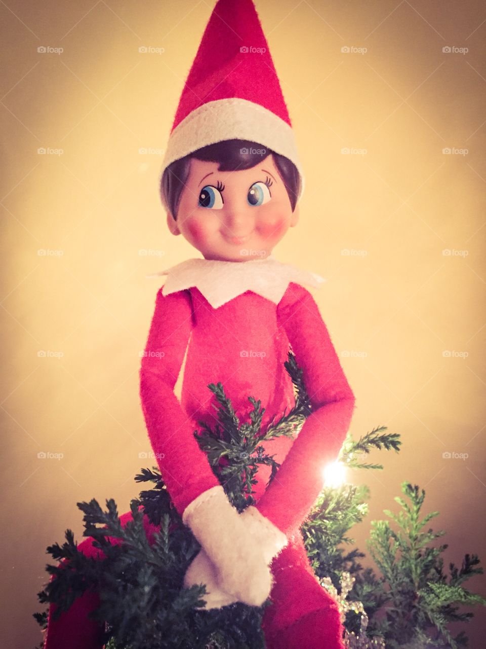 Elf on the shelf sitting atop a Christmas tree.