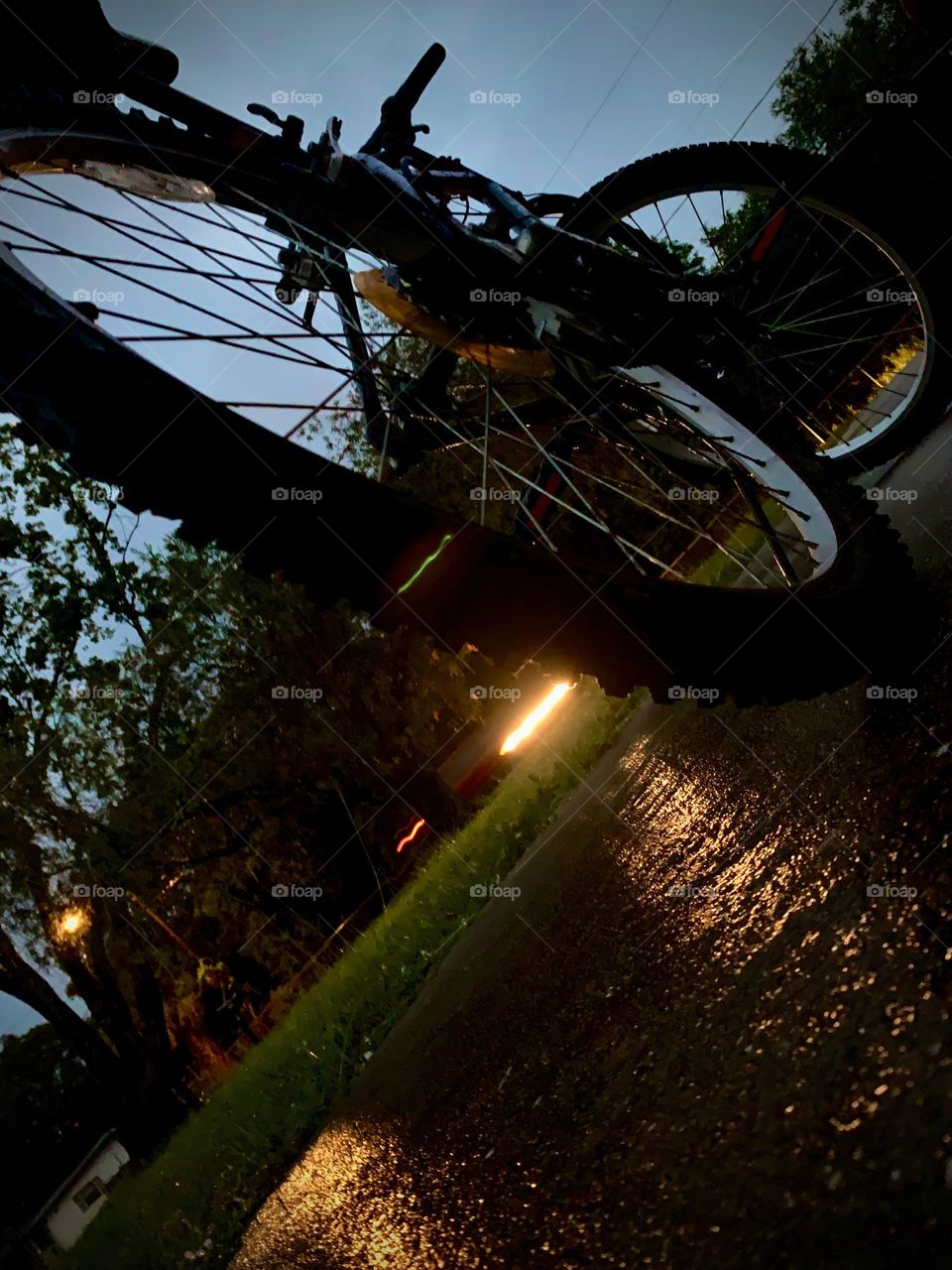 A Lonely Bicycle At Night Against Forgotten But Seen With The Street Light Standing And Close Up On The Wheels While A Car Passing By Unnoticed.