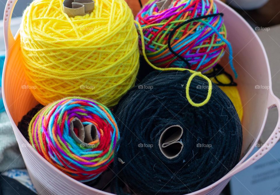A pink basket with colorful spools of yarn up close