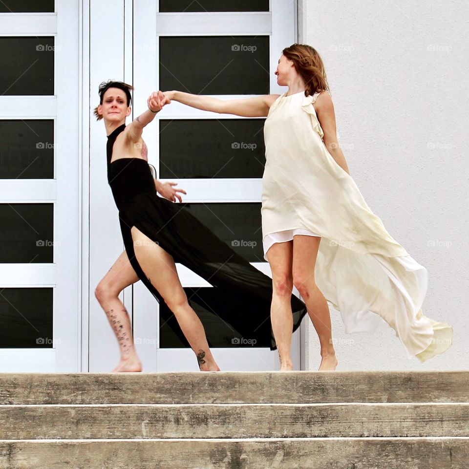 Two women dancing and fluttering in the breeze in front of an urban geometric architectural building.