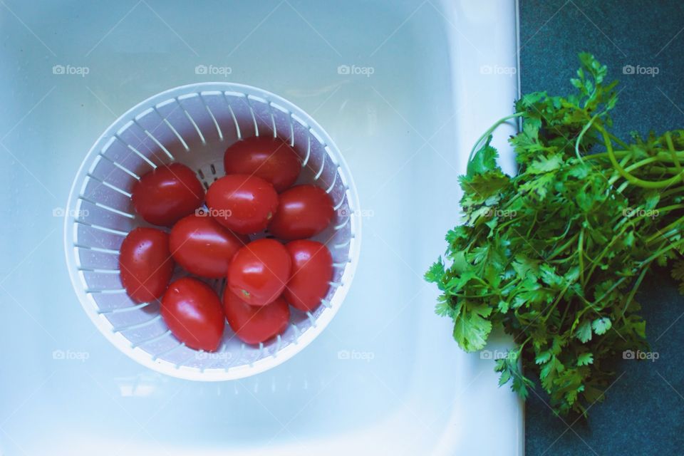 Roma tomatoes in a white colander in a white sink, freshly picked cilantro to the side on a green countertop