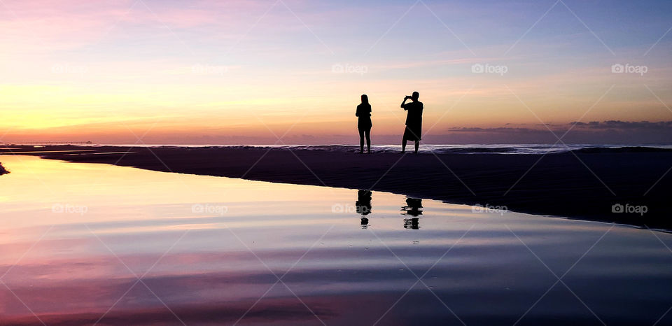 Couple filming beach sunrise.