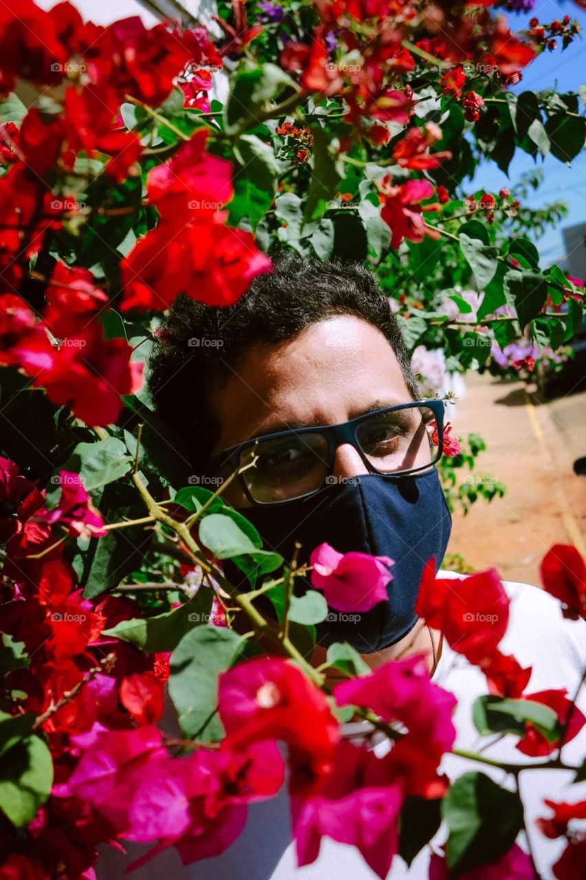 portrait of a Man with Corona Mask On, between red flowers. Hope, hopeful beautiful photo. Glasses and mask on