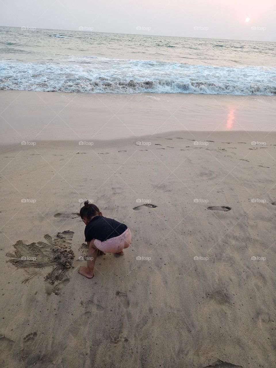 A cute young baby girl playing in the sand at the beach enjoying Holliday