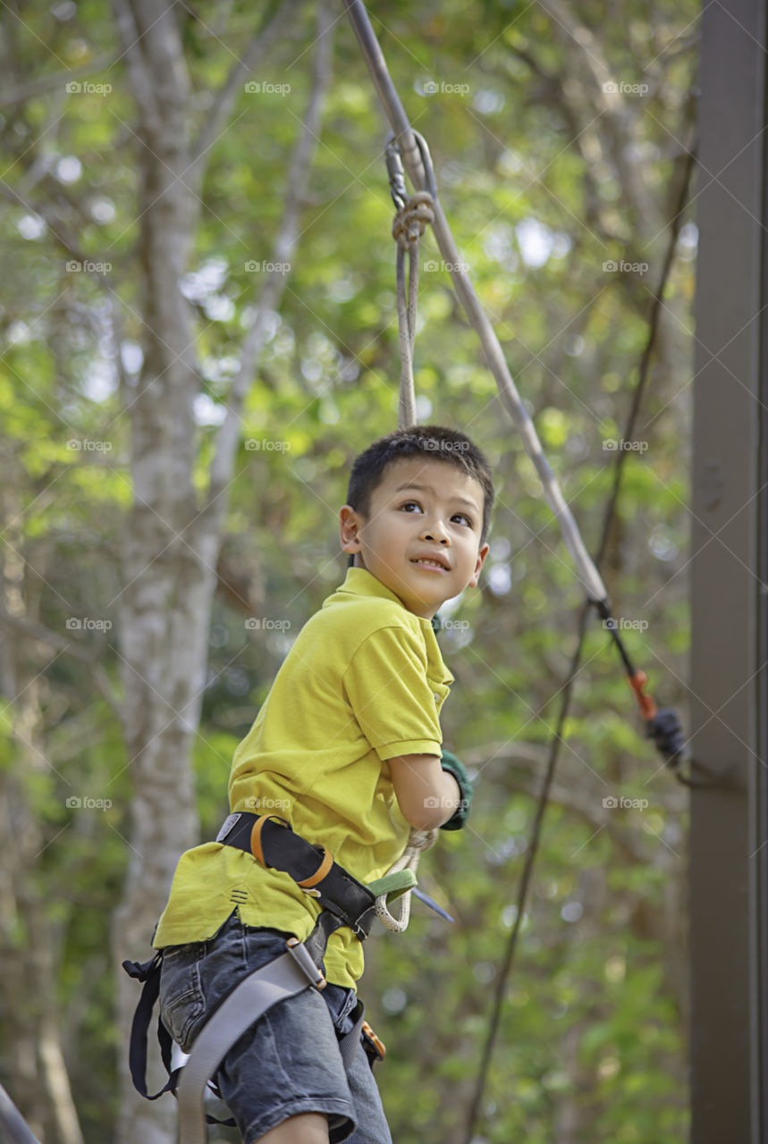 Asean boy nodes the rope and smiling happily in camp adventure Background blurry tree.