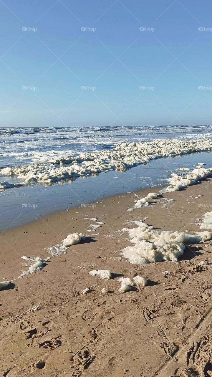 Sea foam from the waves spreading across the beach
