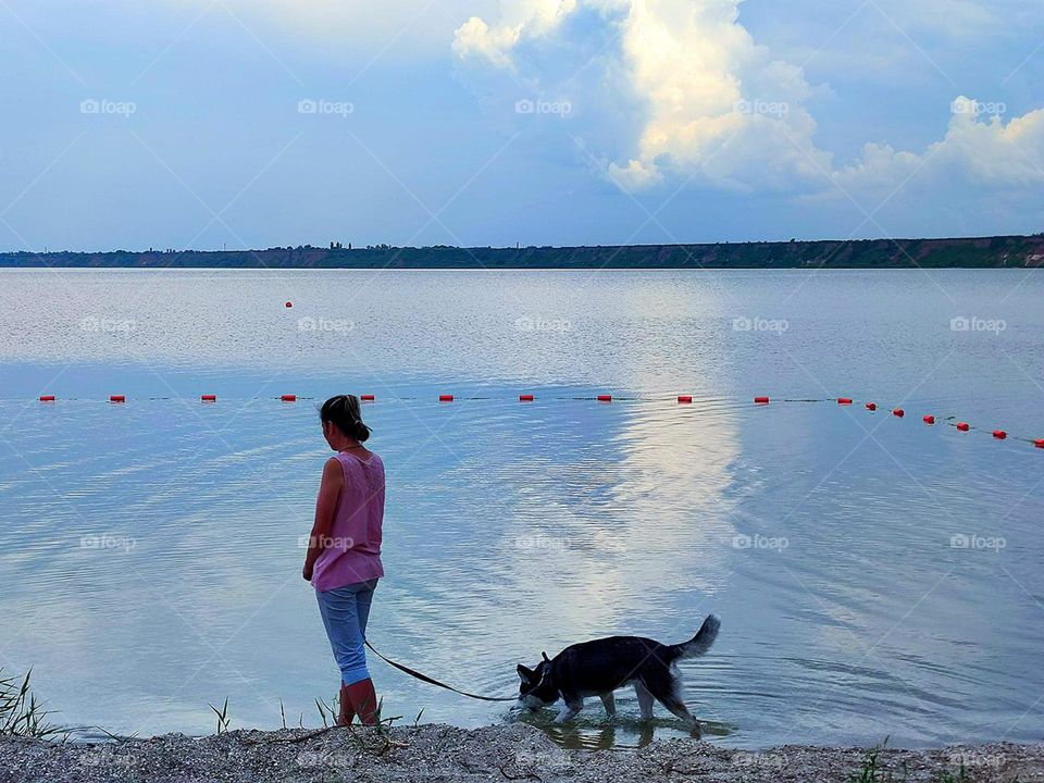 Sea water movement. A woman with a dog is standing on the seashore. In the blue water of the sea a white cloud is reflected in motion
