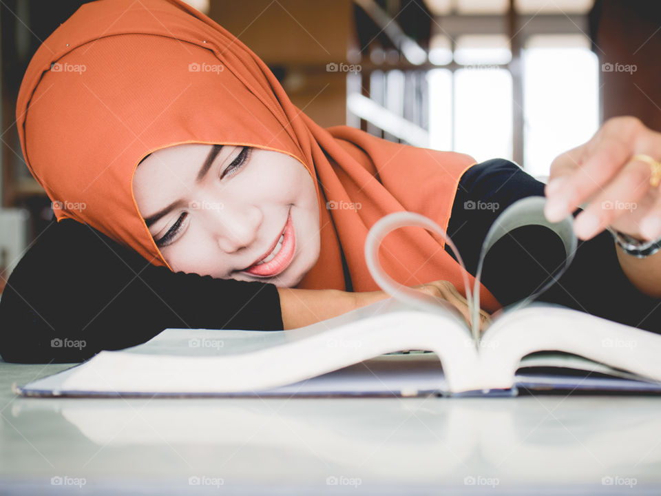 Hijab girl making heart shape with page in book