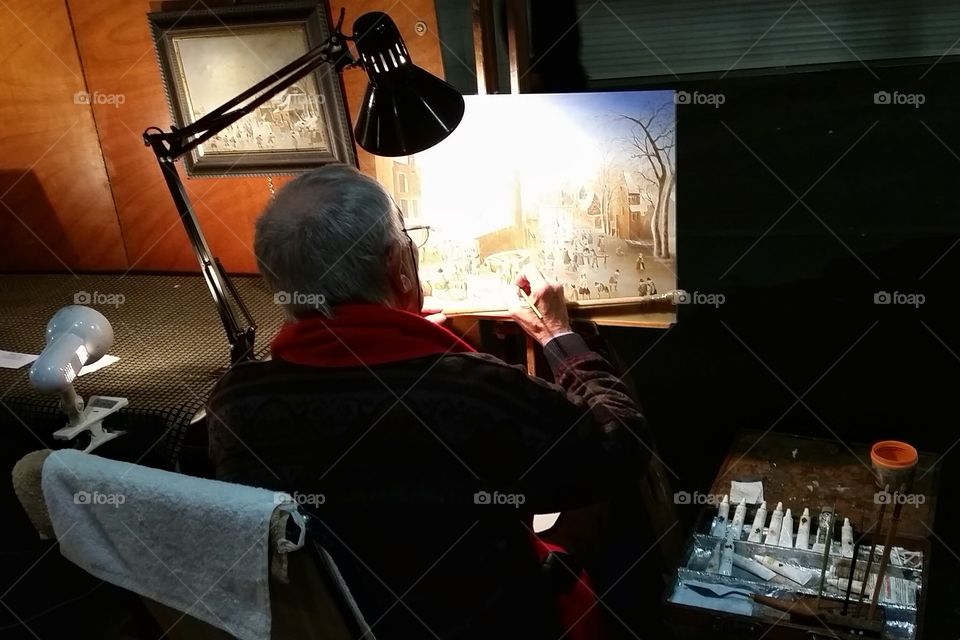An experienced painter is working on his paint under the light on a street of Antibes, France.