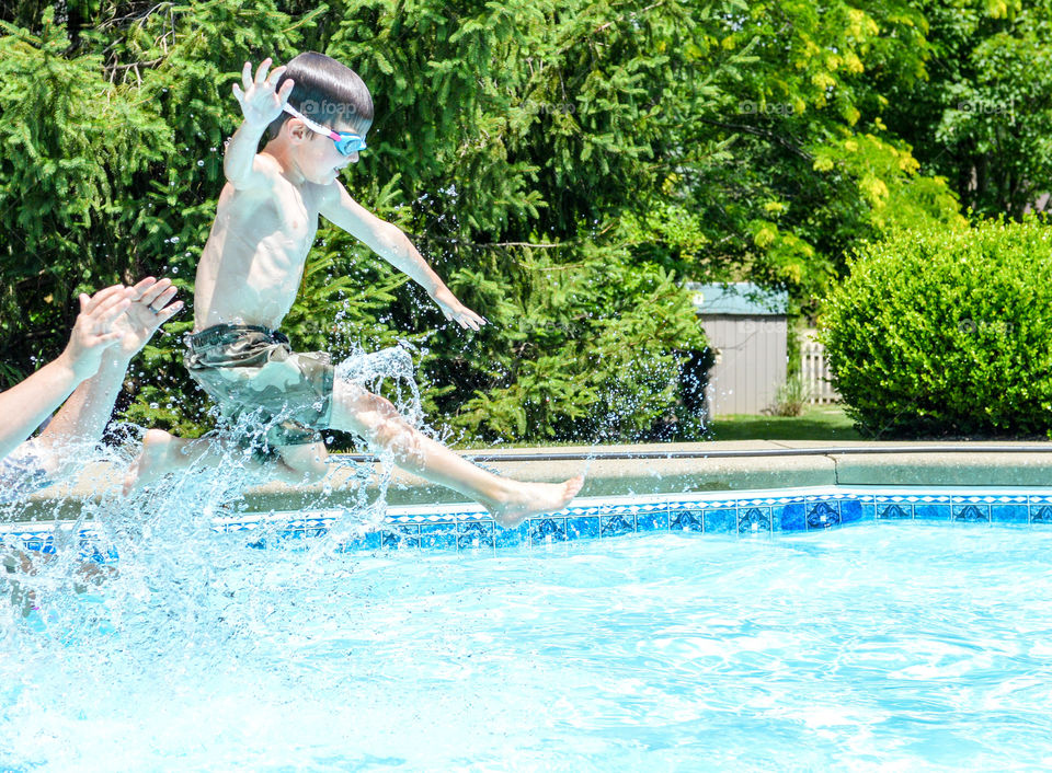 Young boy being thrown into an inground swimming pool and making a splash