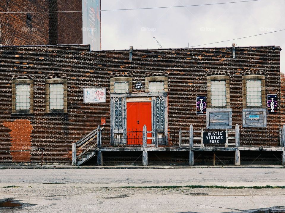 A old brick building tarnished by decades of harsh weather and sunlight is contrasted by a bright red door