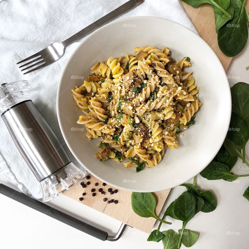 A delicious pasta and sausage meal flat lay displayed with fresh spinach, Parmesan, and peppercorns