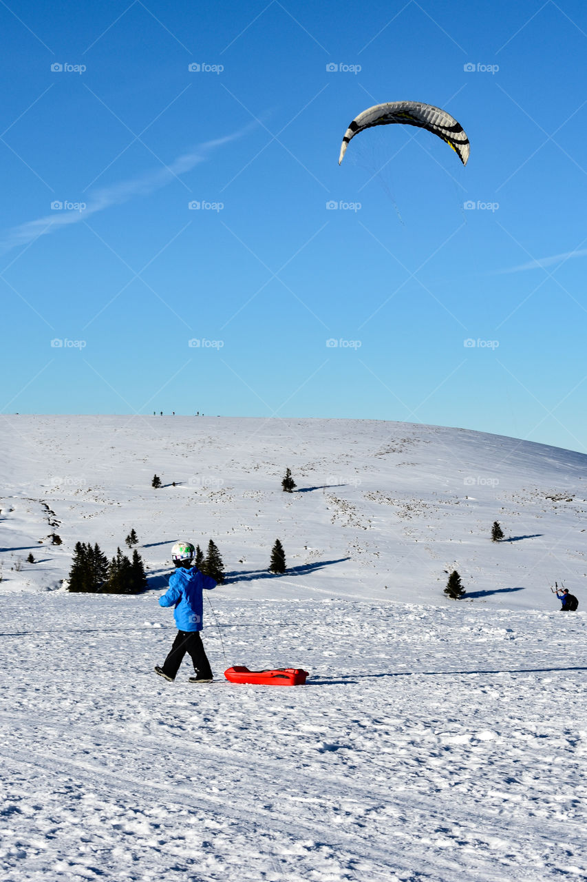 little boy with his red sled in the snow in the mountains