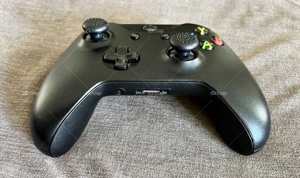 Xbox video game controller that’s black, handheld, has buttons, and joysticks to control a video game on a tv in your living room for entertainment value.