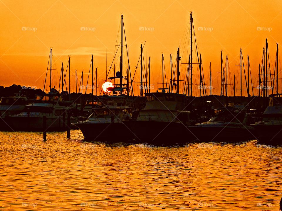 Sunrise, sunset and the moon - At the marina the sailboat sit silently as the golden sun descends below their mask