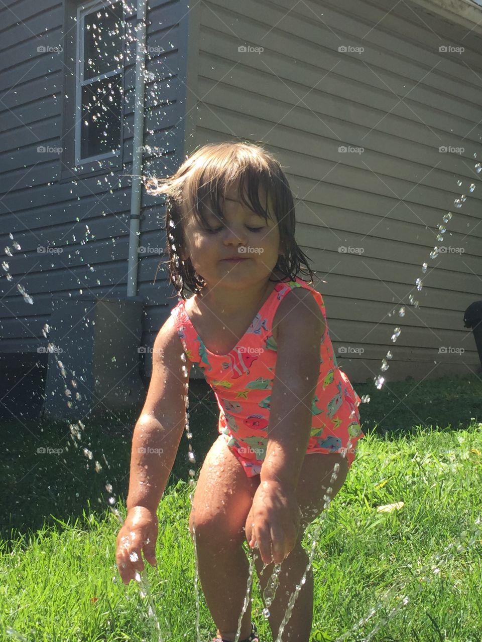 Little girl playing near garden sprinkler